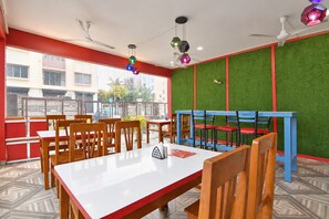 Interior de restaurante con una mesa blanca, sillas de madera, un banco azul y rojo, y una pared verde con una franja roja.