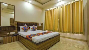 A bedroom with a large bed, a headboard, a bedside table, a mirror, and a window with curtains.