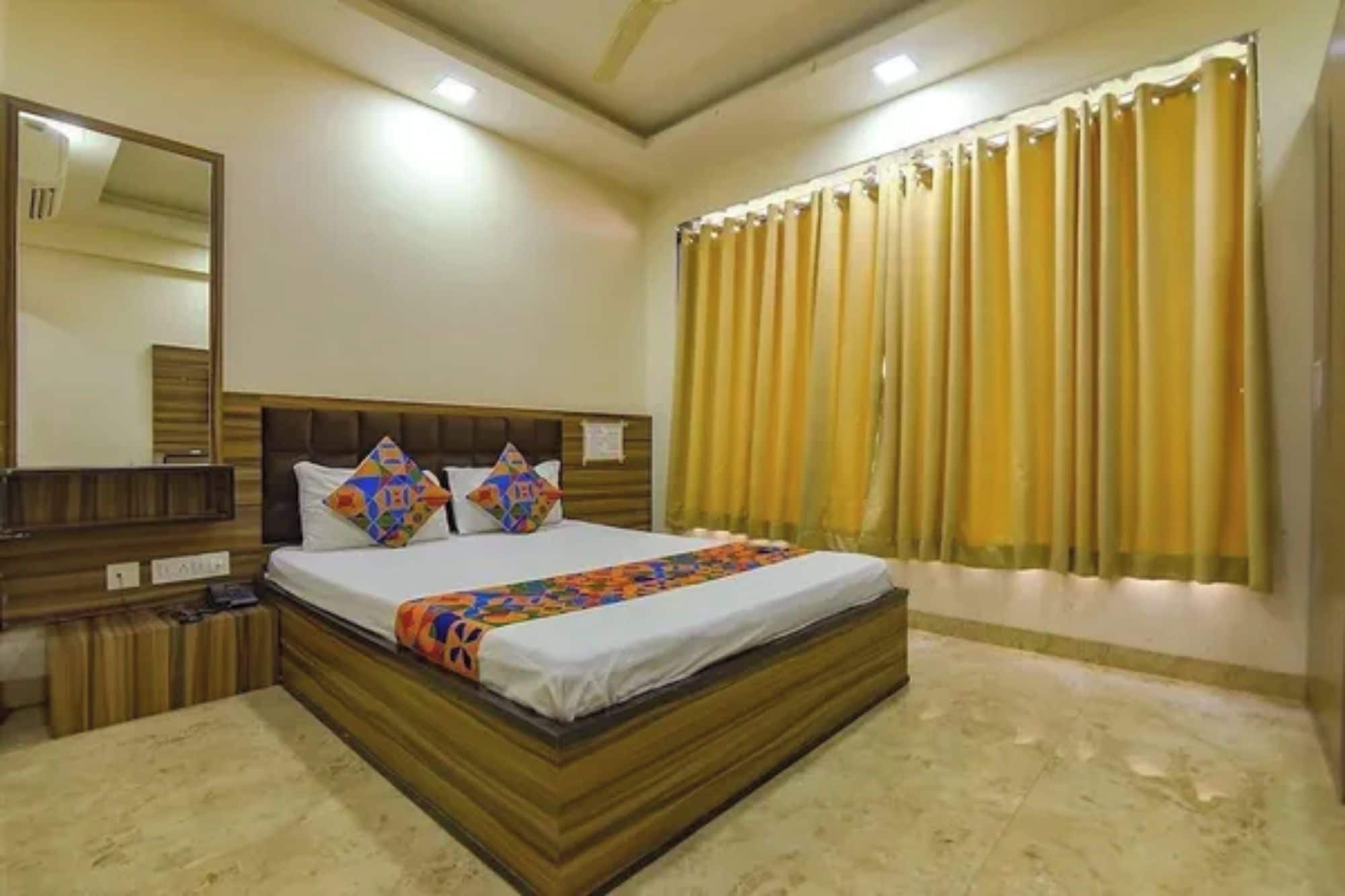 A bedroom with a large bed, a headboard, a bedside table, a mirror, and a window with curtains.