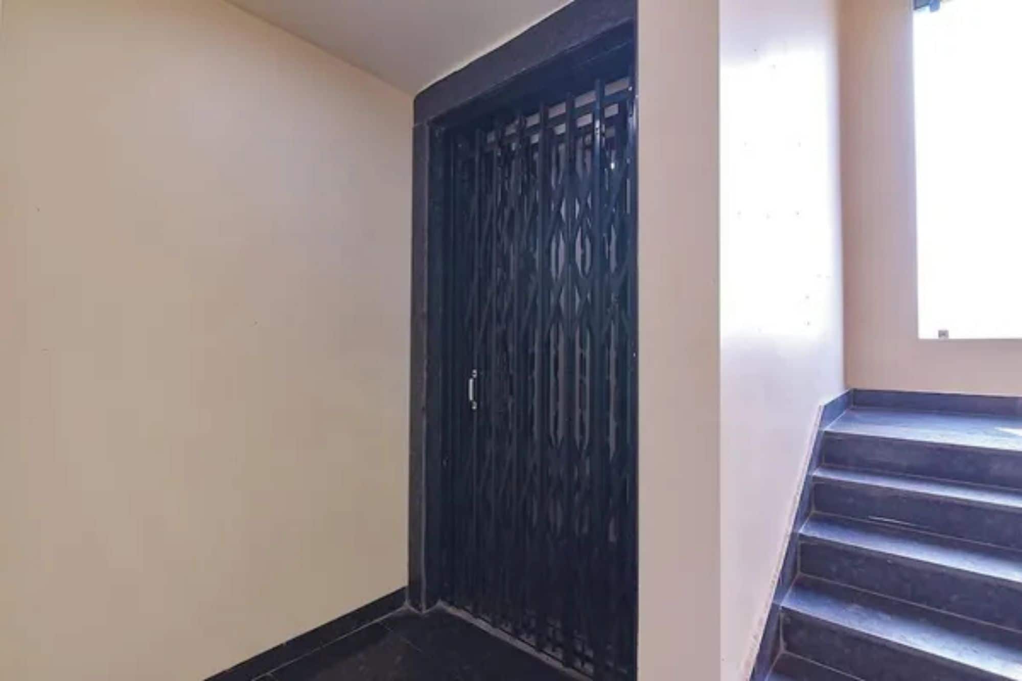 A dark-colored door with a metal grille, a staircase with dark steps, and a plain wall.