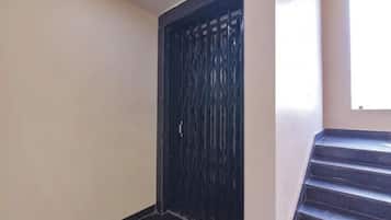A dark-colored door with a metal grille, a staircase with dark steps, and a plain wall.