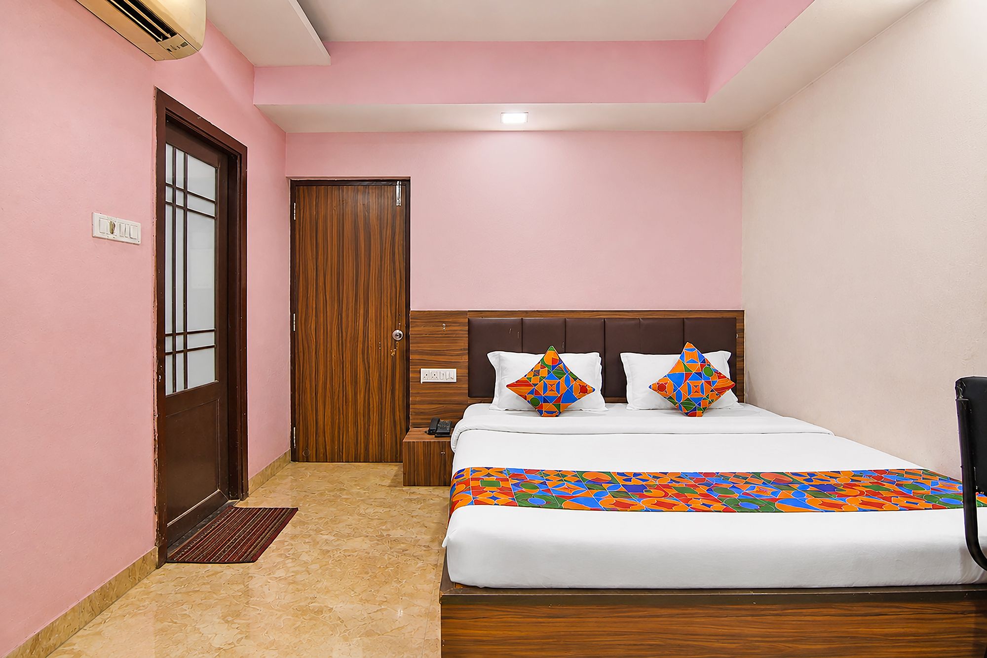 Un dormitorio con una cama, una mesita de noche, una puerta de madera y un aire acondicionado instalado en la pared.