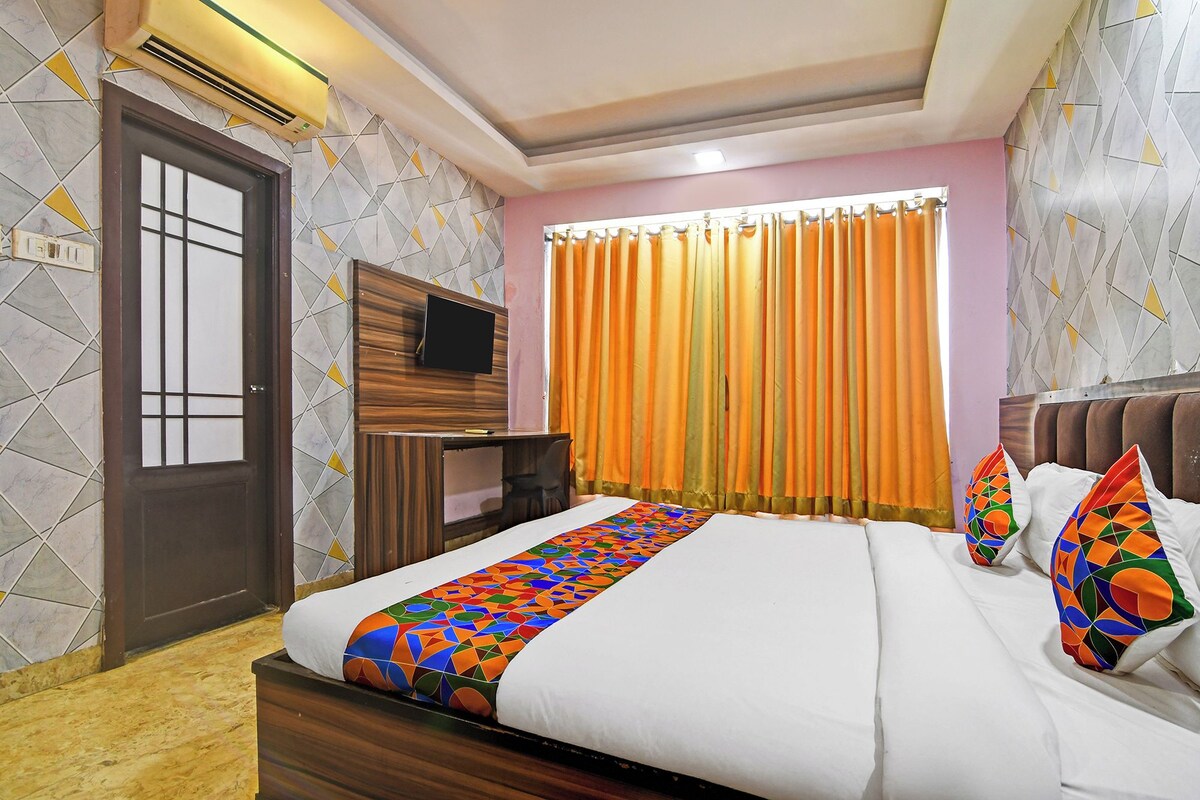 Una habitación de hotel con una cama, un televisor sobre un soporte de madera, una ventana con cortinas naranjas y una pared con diseño.