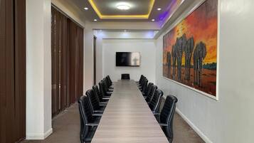 Un salón de conferencias con una larga mesa y sillas, un televisor de pantalla plana montado en la pared y un cuadro en la pared derecha.