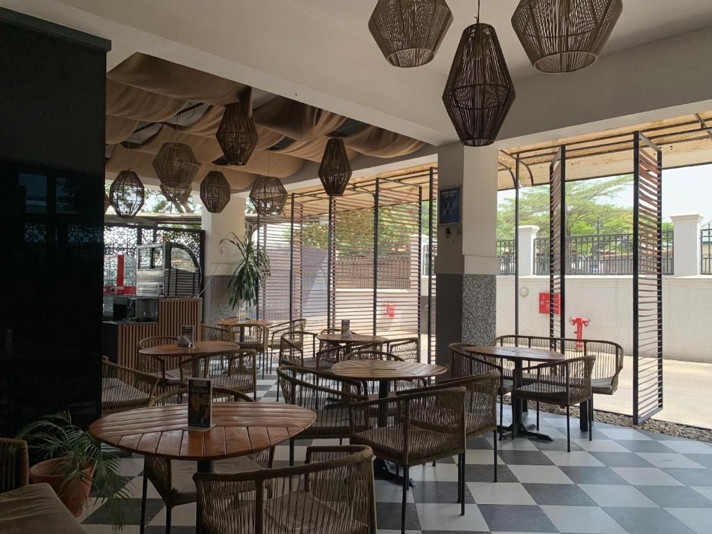 An indoor seating area with round tables and wicker chairs, featuring a checkered floor and hanging wicker lamps.