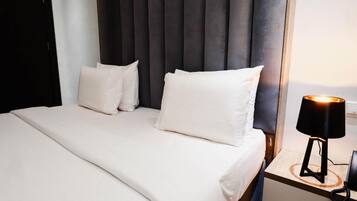 A neatly made bed with white linens and pillows, a bedside lamp, and a dark headboard.