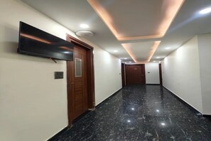 Un pasillo con una televisión de pantalla plana montada en la pared, puertas de madera y suelo de mármol.