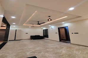 Amplia habitación con techo alto, iluminación empotrada, ventilador de techo y sofá negro.
