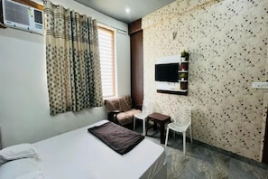 A bedroom with a bed, a small table, a chair, a TV, and a window with curtains.
