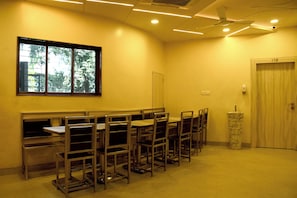 Un aula con escritorios y sillas dispuestas en filas, una ventana con vistas a árboles, una puerta y un ventilador de techo.