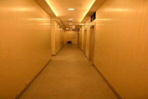 Un estrecho pasillo de hotel con puertas a ambos lados, suelo de baldosas e iluminación empotrada.
