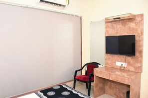 Una habitación con una pizarra, un escritorio con televisor, una silla roja y una alfombra estampada.