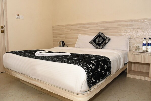 Habitación de hotel con una cama, una mesita de noche con hervidor y una mesita de noche con botellas de agua.