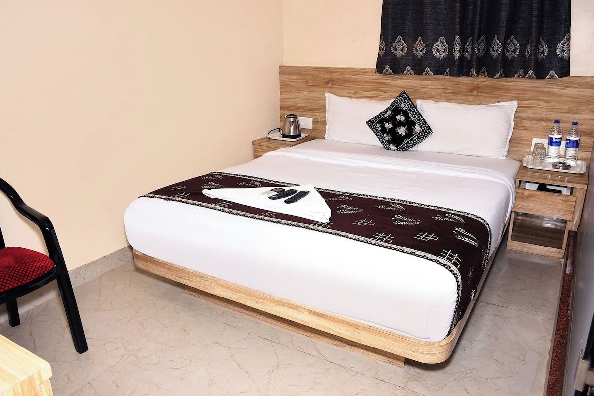 Habitación de hotel con cama, mesita de noche, una silla y ventana con cortinas.