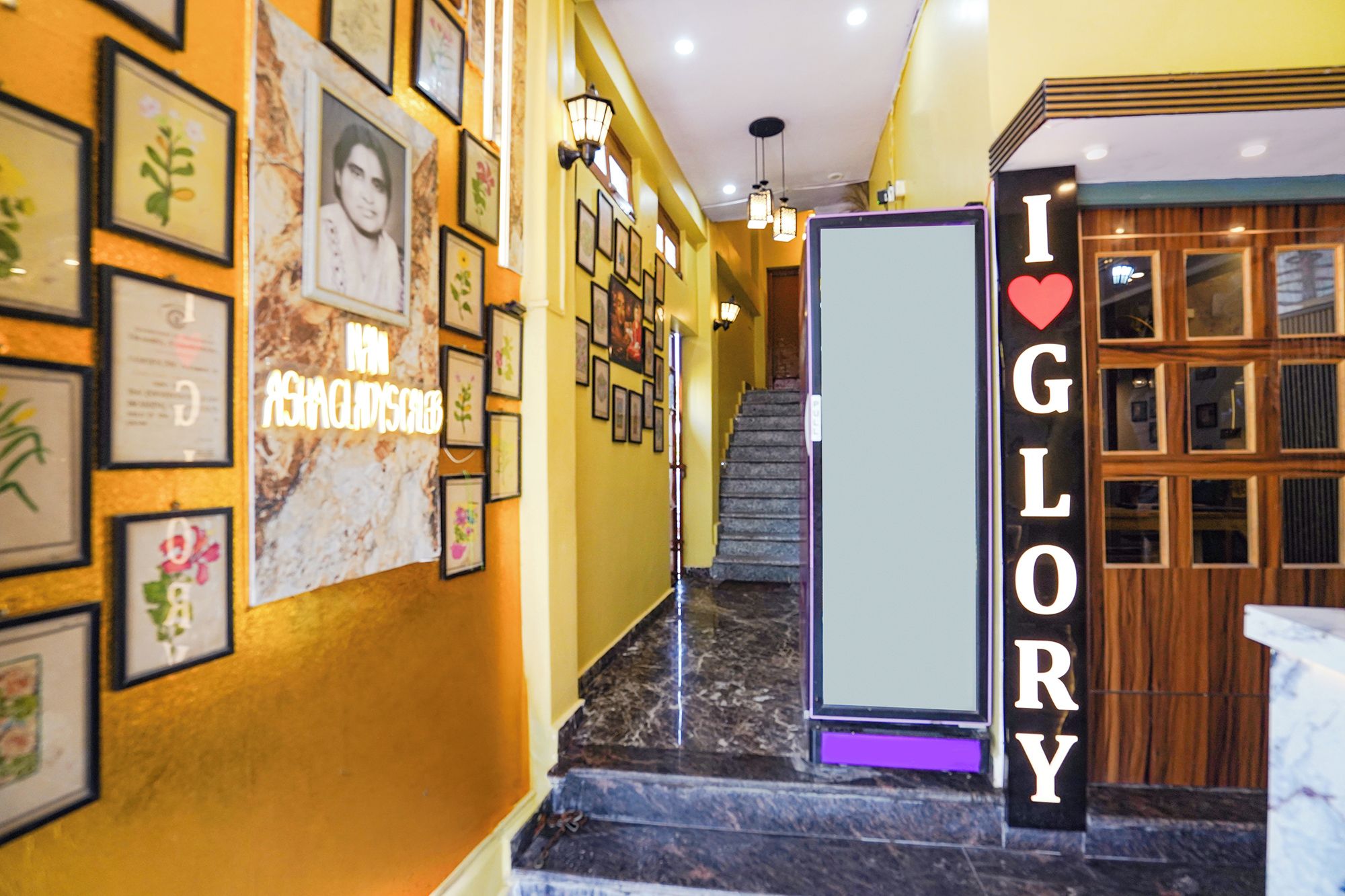 Un vestíbulo de hotel con una escalera, cuadros en las paredes y un letrero que dice 'I ♥ GLORY'.