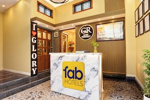 Zona de recepción de un hotel con mostrador de mármol, un cartel de 'fab hotels' y un letrero que indica 'GR GLORY RESIDENCY' sobre la entrada.