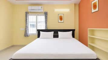 A hotel room with a bed, an air conditioning unit, a window with curtains, a wall-mounted shelf, and a framed picture.