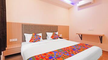 Una habitación de hotel con cama, mesita de noche, aire acondicionado instalado en la pared y una pequeña estantería.
