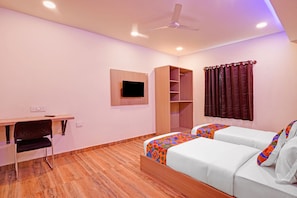 Una habitación de hotel con cama, escritorio, silla, armario, televisor y ventilador de techo.