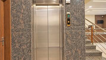 Un ascensor con pantalla digital, flanqueado por paredes de granito y una puerta de madera.