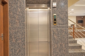 Un ascensor con pantalla digital, flanqueado por paredes de granito y una puerta de madera.