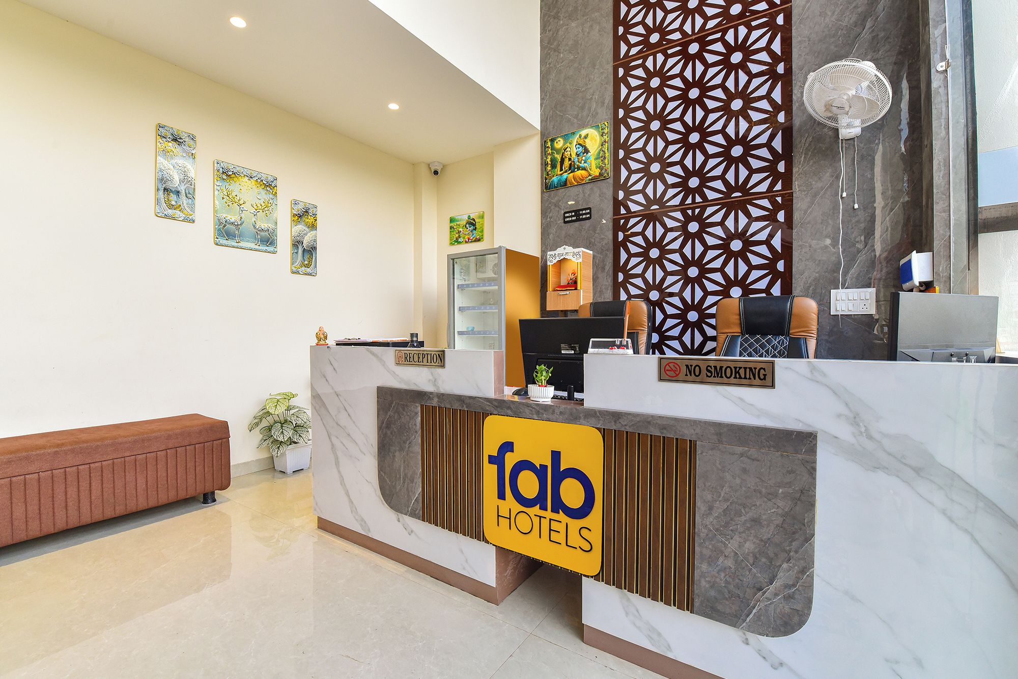 Zona de recepción de hotel con mostrador de mármol, una mesa de recepción, un cartel de 'No Fumar' y obras de arte enmarcadas en la pared.