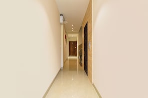 Un pasillo estrecho con una puerta de madera al final, un equipo de aire acondicionado en la pared y un pasamanos a la derecha.