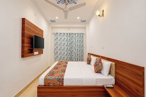 Habitación de hotel con cama, televisor montado en la pared, ventilador de techo y ventana con cortinas.