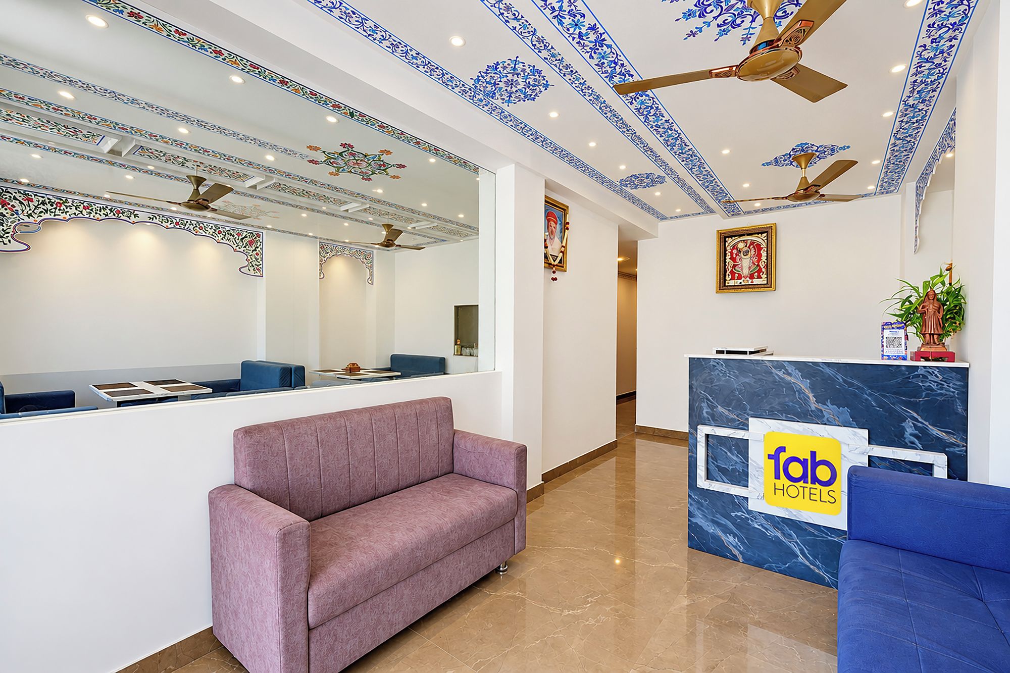 Zona de recepción de hotel con un mostrador de mármol, un sofá morado y un ventilador de techo.