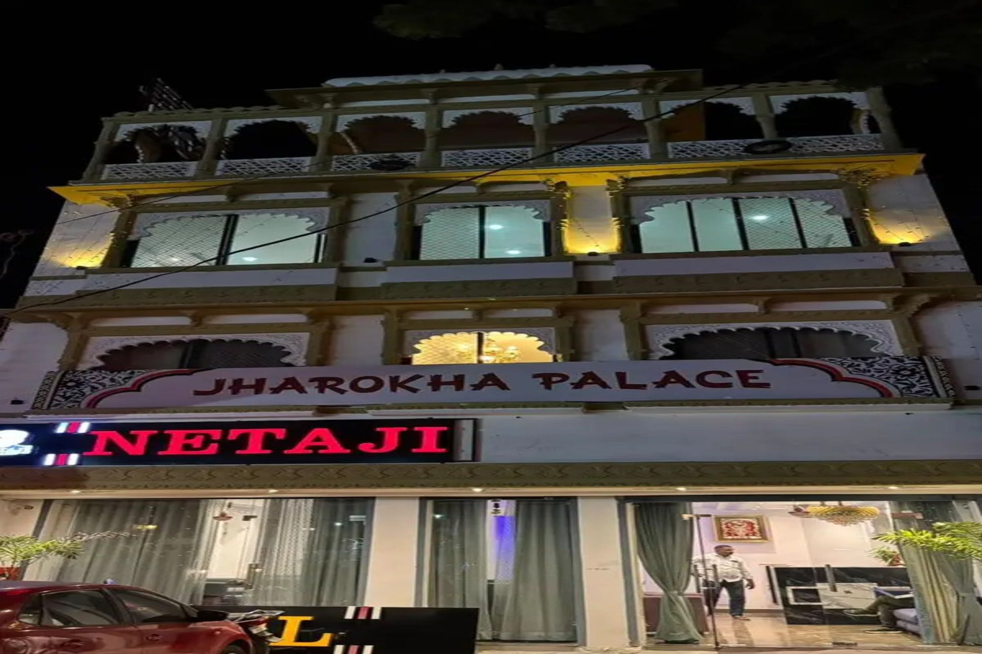 Un edificio de varios pisos con un letrero que dice 'JHAROKHA PALACE' y una tienda con un letrero que dice 'NETAJI'.