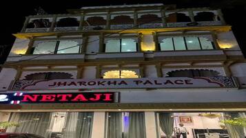 Un edificio de varios pisos con un letrero que dice 'JHAROKHA PALACE' y una tienda con un letrero que dice 'NETAJI'.