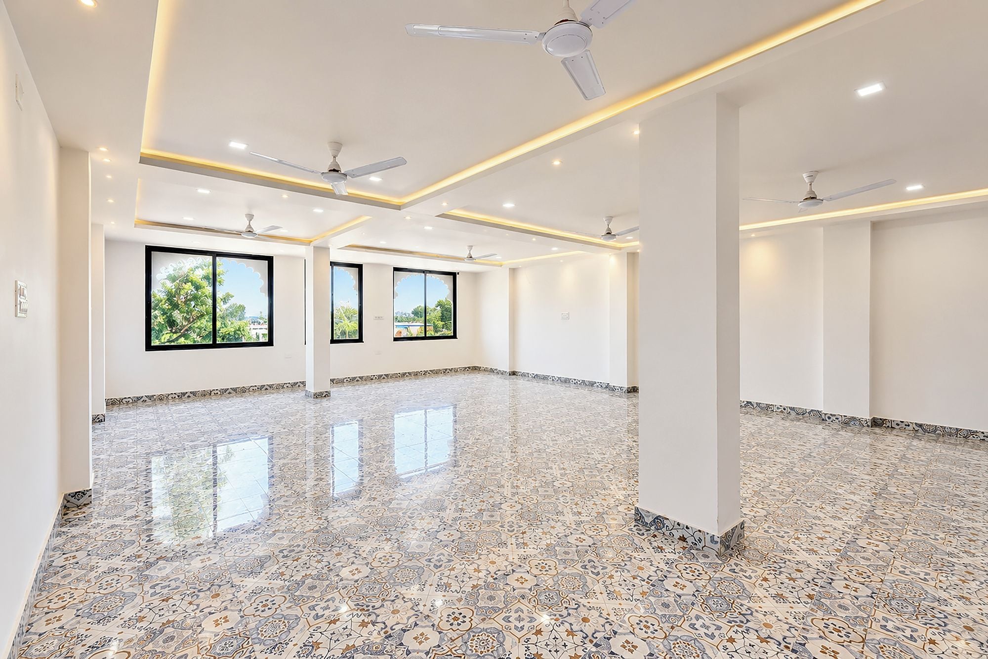 Una habitación amplia con piso pulido, ventanas grandes y ventiladores de techo.