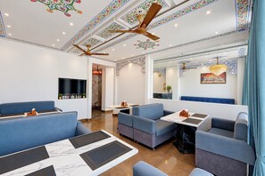 A modern dining area with blue upholstered seating, a flat-screen TV, and decorative ceiling patterns.