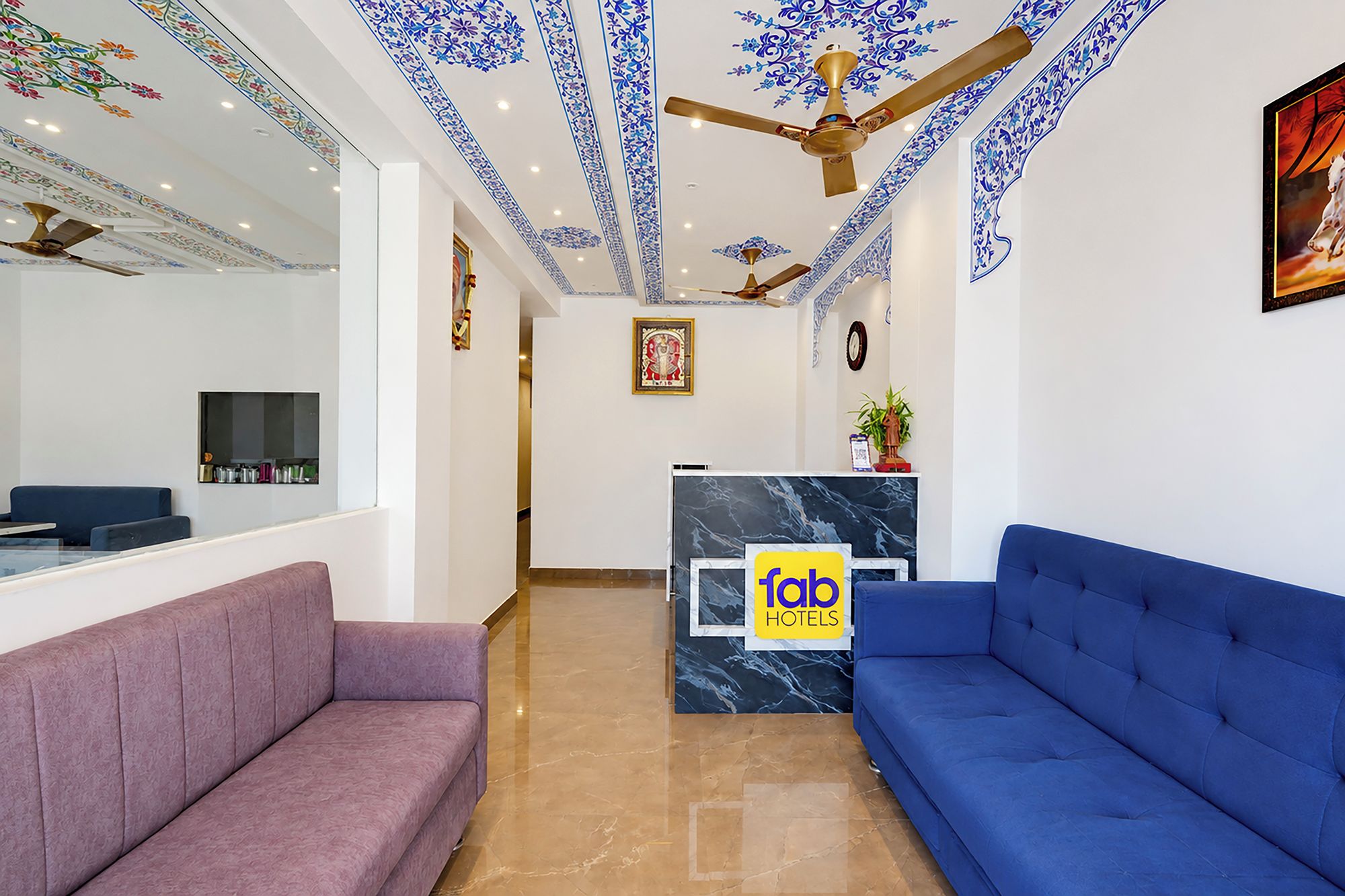 A hotel reception area with a marble counter, a reception desk, a blue sofa, a purple sofa, and decorative ceiling patterns.