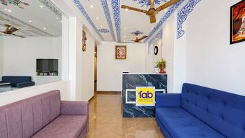 A hotel reception area with a marble counter, a reception desk, a blue sofa, a purple sofa, and decorative ceiling patterns.