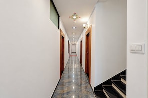 Un pasillo de hotel con suelo de mármol, puertas de madera y una escalera a la derecha.
