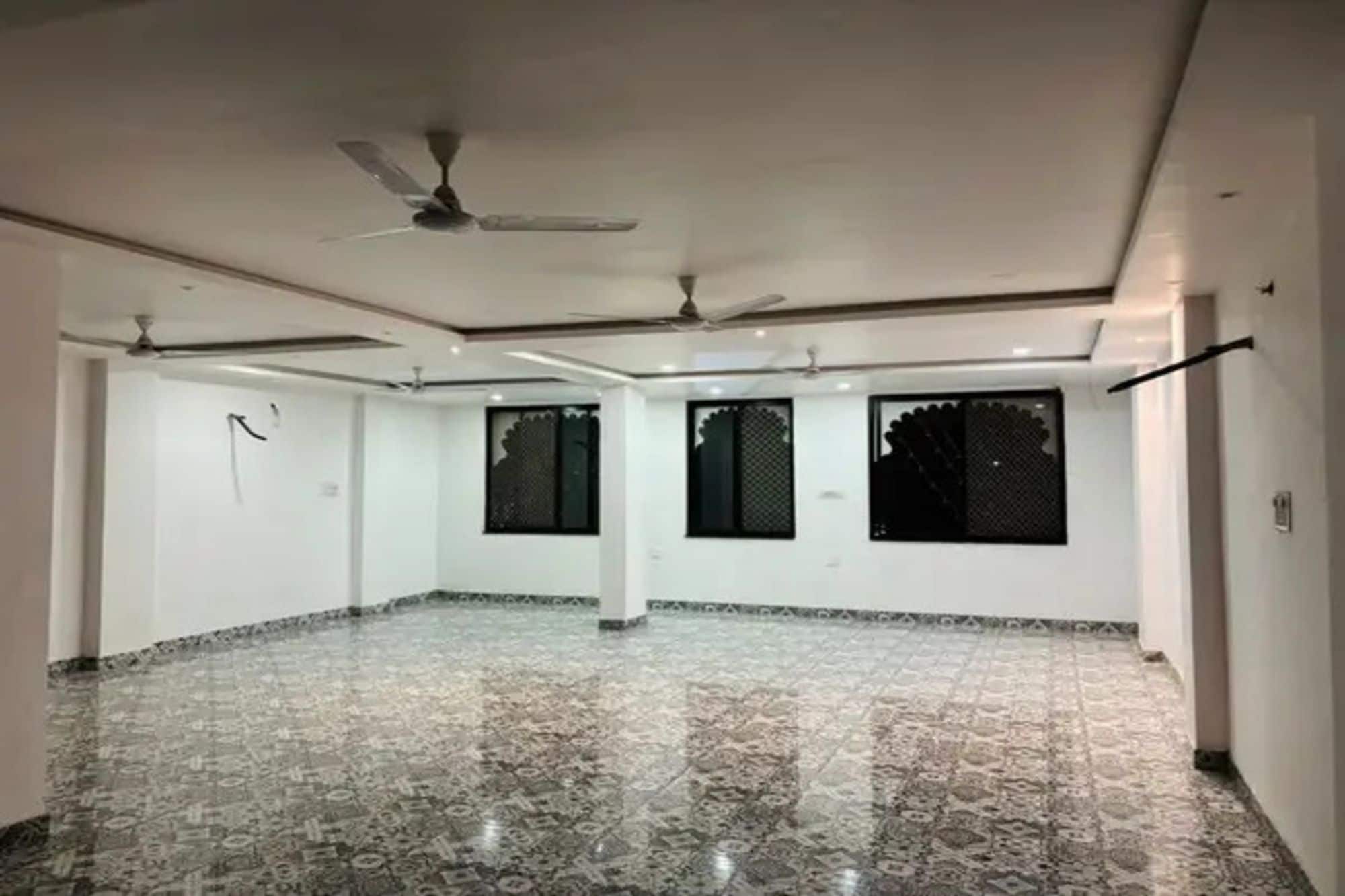 Amplia habitación con piso de mármol, ventiladores de techo y ventanas grandes.
