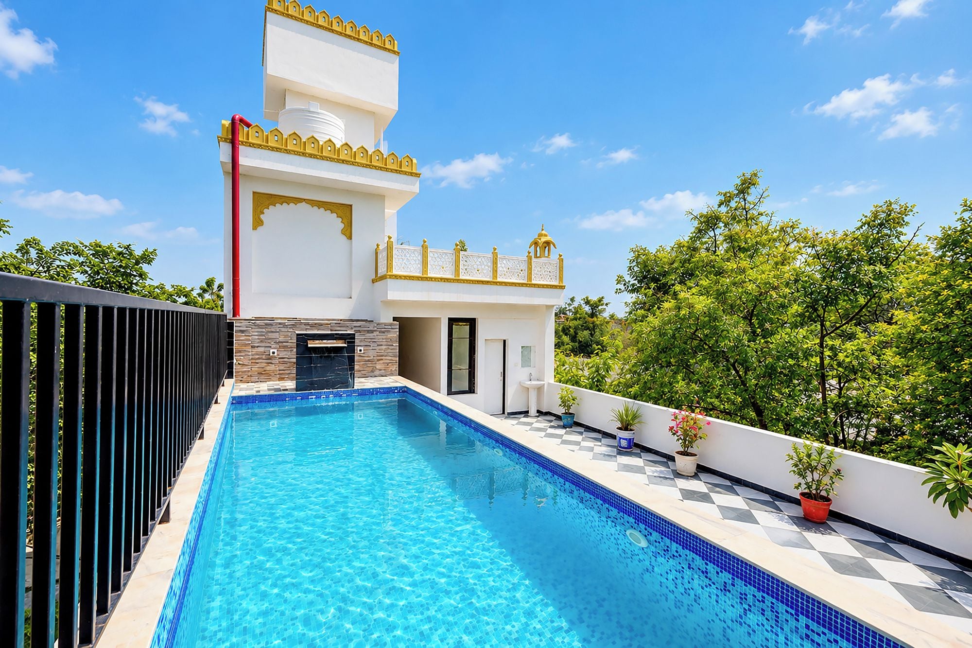 Ein moderner Poolbereich mit einem klaren, blauen Pool, einem weißen Gebäude mit gelben Akzenten und üppigem Grün im Hintergrund.