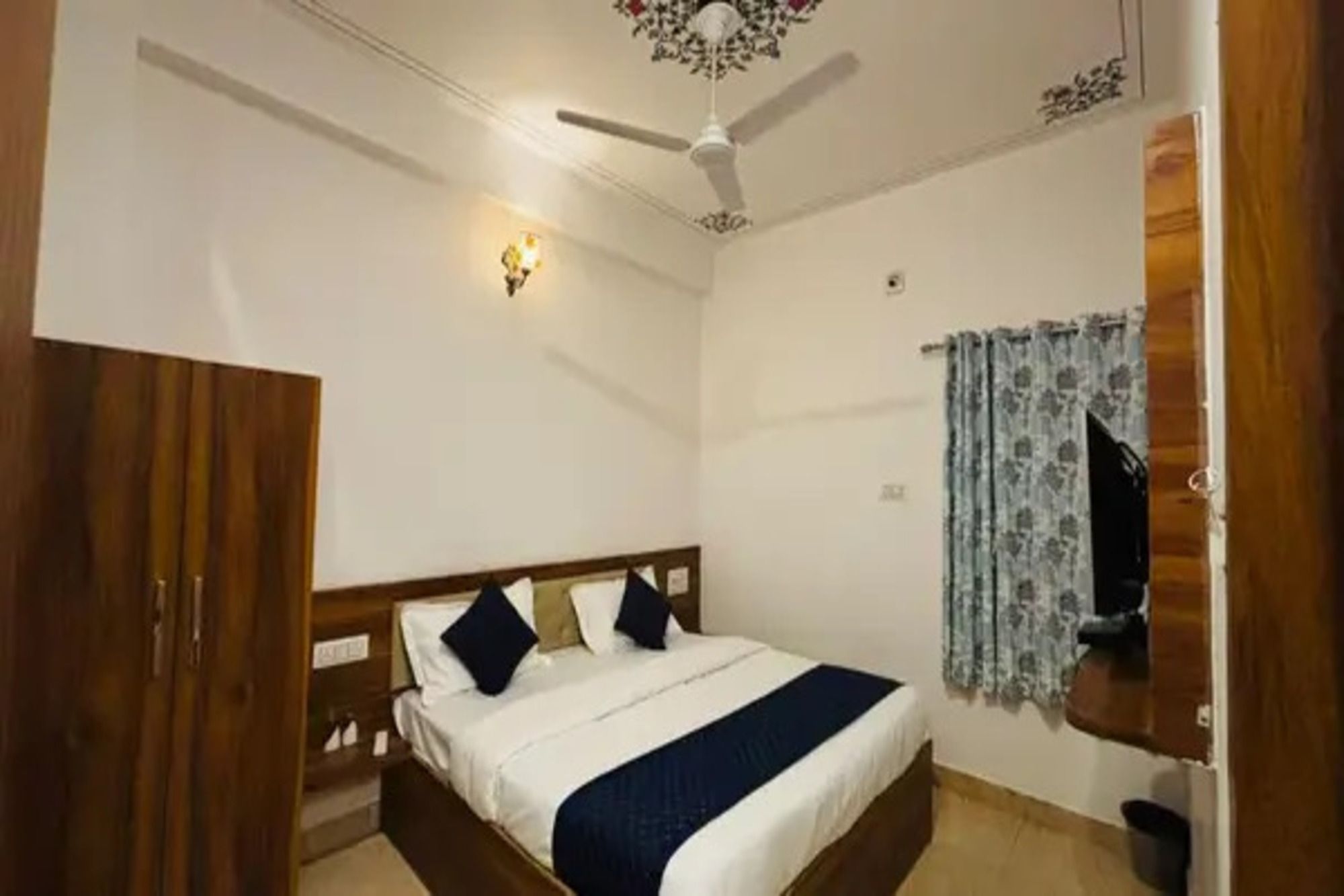 Un dormitorio con cama, ventilador de techo, luz empotrada en la pared y ventana con cortinas.