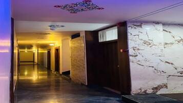 Pasillo de hotel con pared de mármol, una puerta con ventanal y techo decorado con motivos florales.