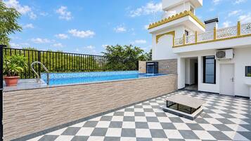 A swimming pool with a checkered floor, a potted plant, and a building with a white facade and yellow trim.