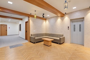 A modern lobby with a herringbone floor, a sectional sofa, a wooden coffee table, a ceiling fan, and an elevator.