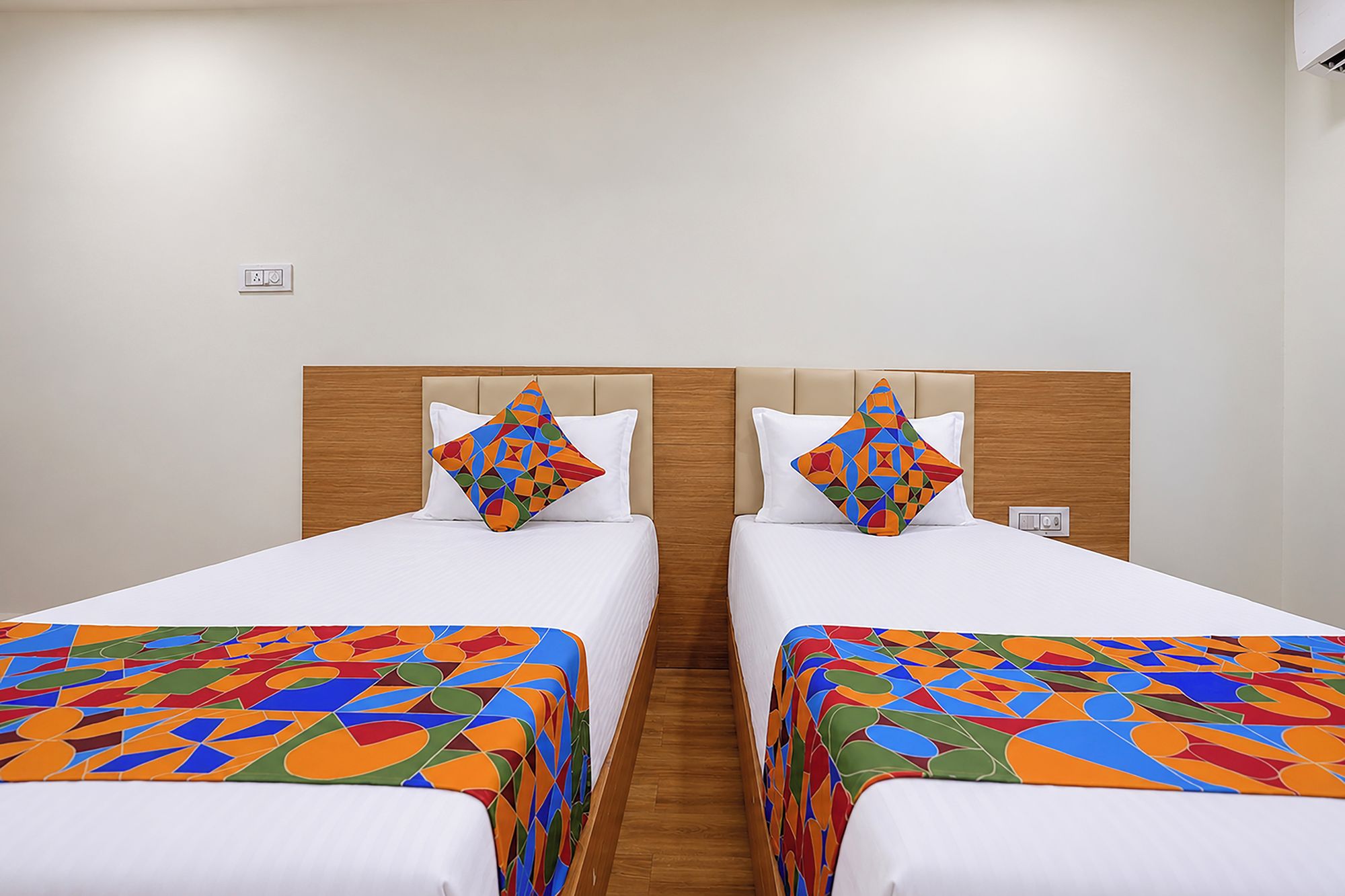 Habitación de hotel con dos camas, cada una con un edredón y almohadas a juego de estampado geométrico colorido.