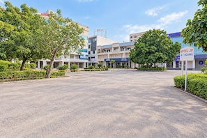 A hotel entrance with a paved driveway, trees, and a building with signage for 'Hotel JP' and 'A.C. Rooms'.