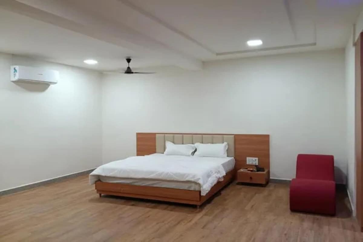 Quarto com cama de madeira, mesa de cabeceira, cadeira vermelha e ventoinha no teto.