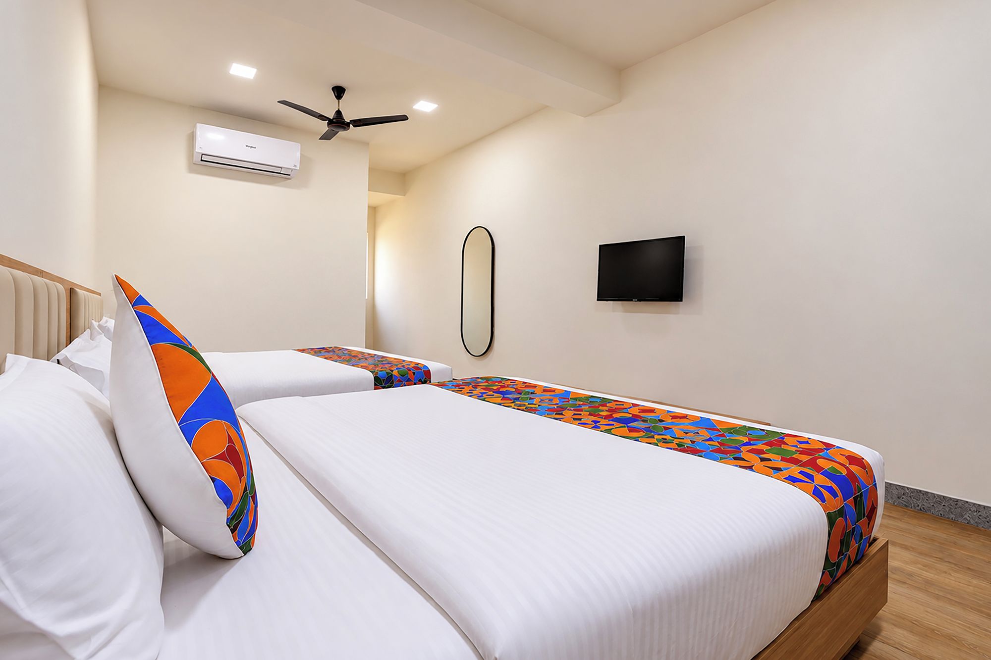 Hotelkamer met een bed, een plafondventilator, een airconditioner, een flatscreen televisie en een spiegel.