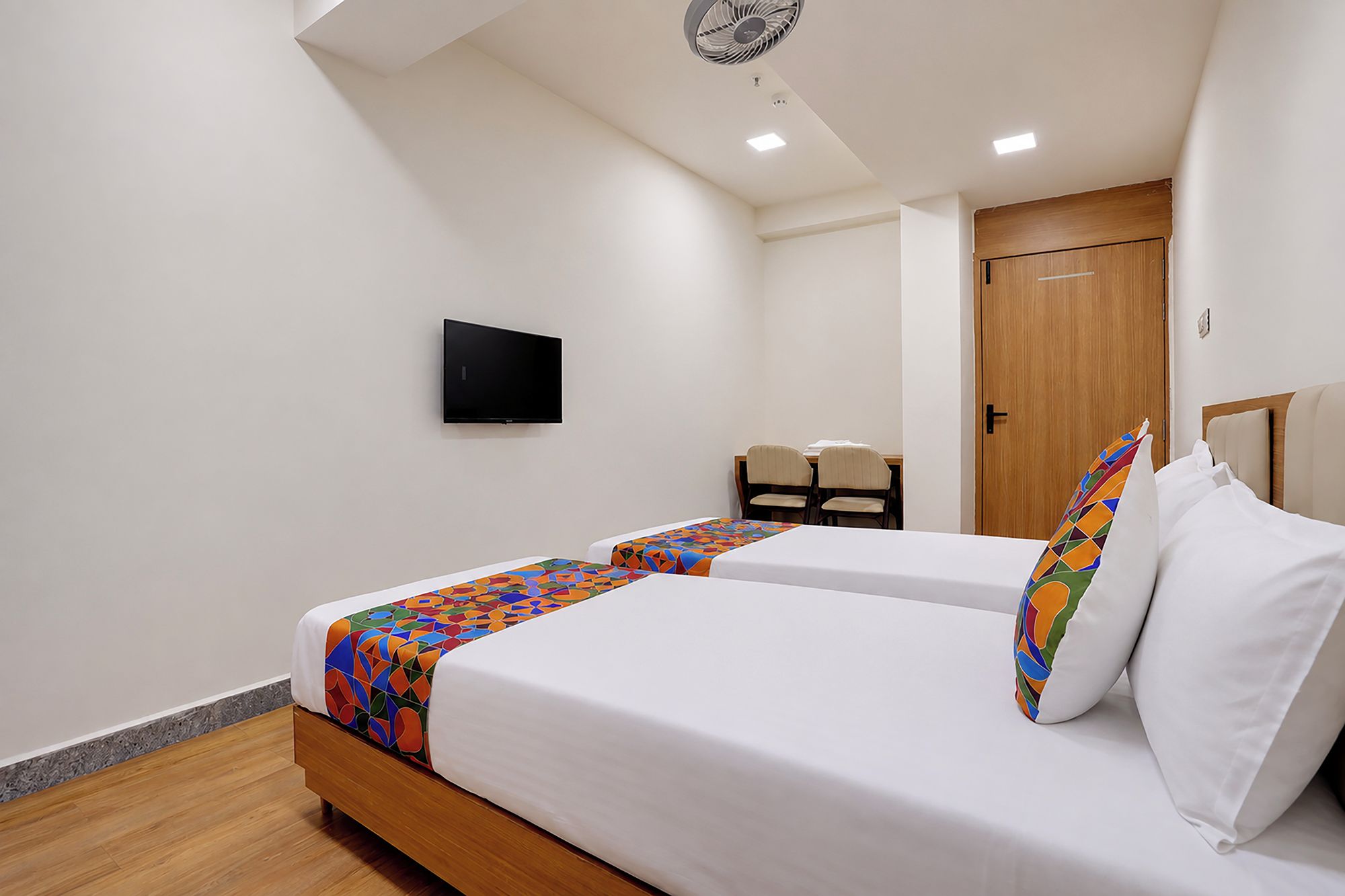 A hotel room with two beds, a TV, a desk with chairs, and a wooden door.