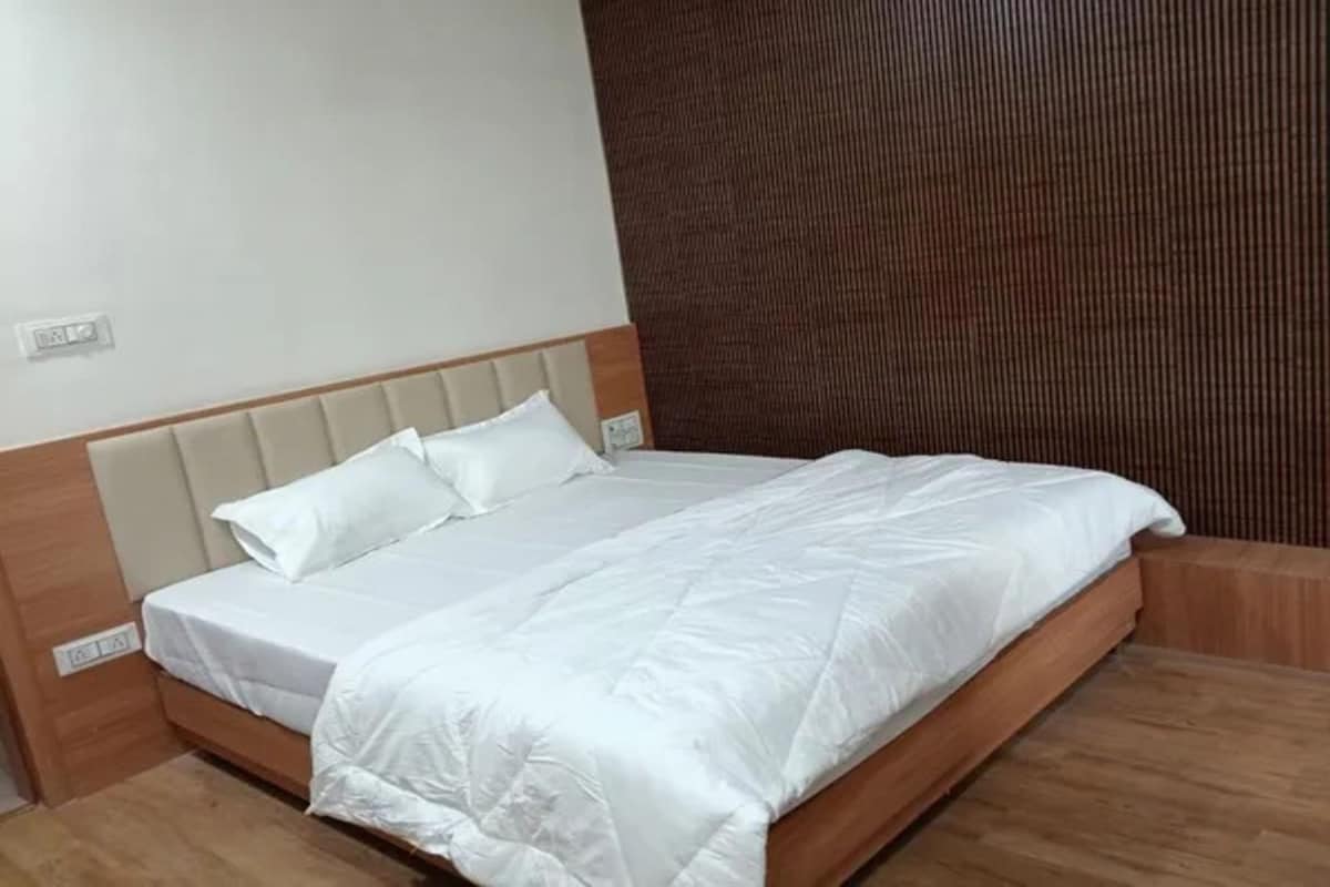 Uma cama de solteiro com cabeceira, roupa de cama branca e piso de madeira.
