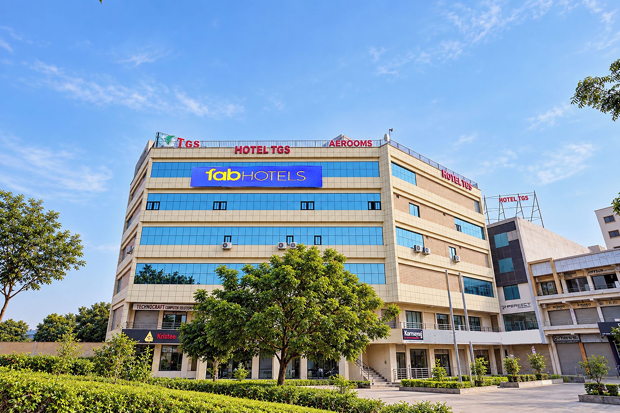 A multi-story hotel with 'HOTEL TGS' signage, 'fabHOTELS' branding, and various commercial establishments on the ground floor.