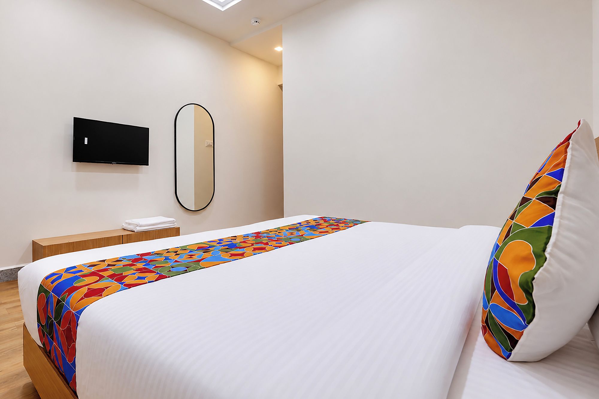 A hotel room with a bed, a bedside table, a flat-screen TV mounted on the wall, and a mirror.